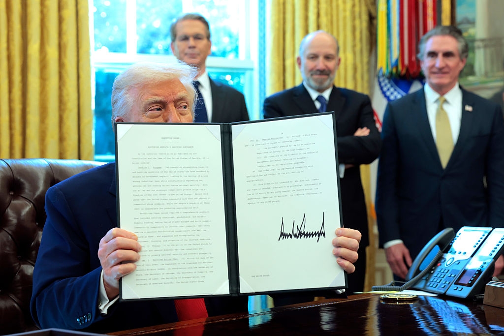 Person at a desk holds up a signed executive document with others standing behind, in an official setting