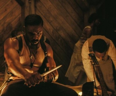 Una escena de película muestra a un hombre sosteniendo un cuchillo mientras otro ajusta su guitarra en un ambiente rústico