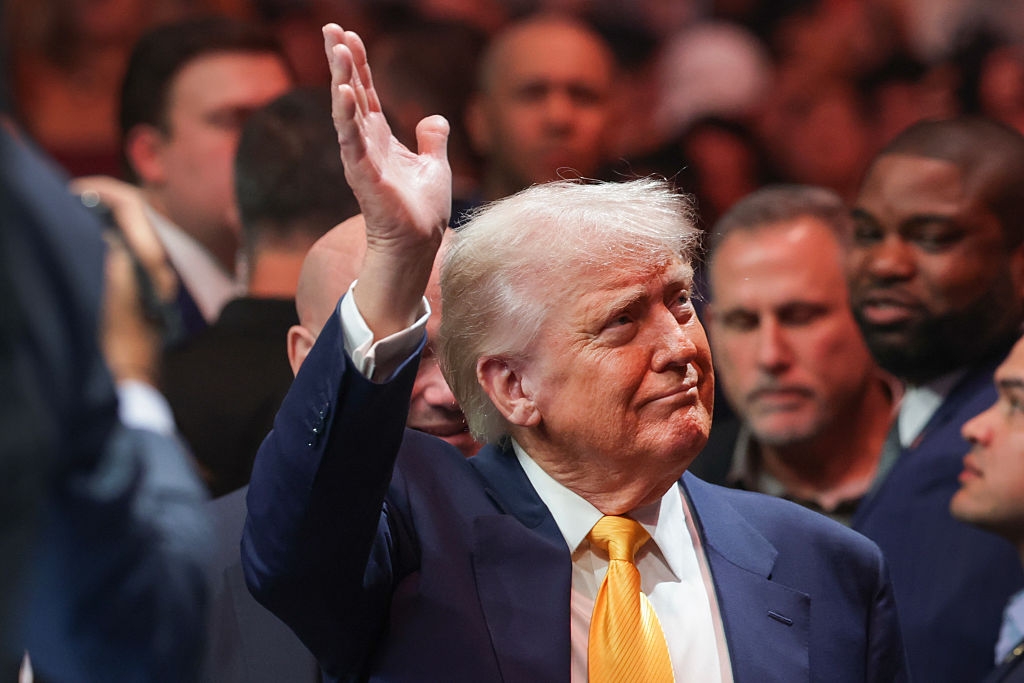 A man in a suit gestures with his hand raised at a crowded event