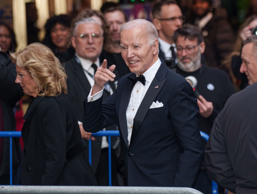 A person in a formal suit points while walking through a crowd at a public event