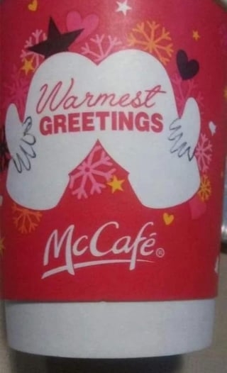 A red McCafé cup with the text "Warmest Greetings," decorated with snowflakes, hearts, and mittens graphic