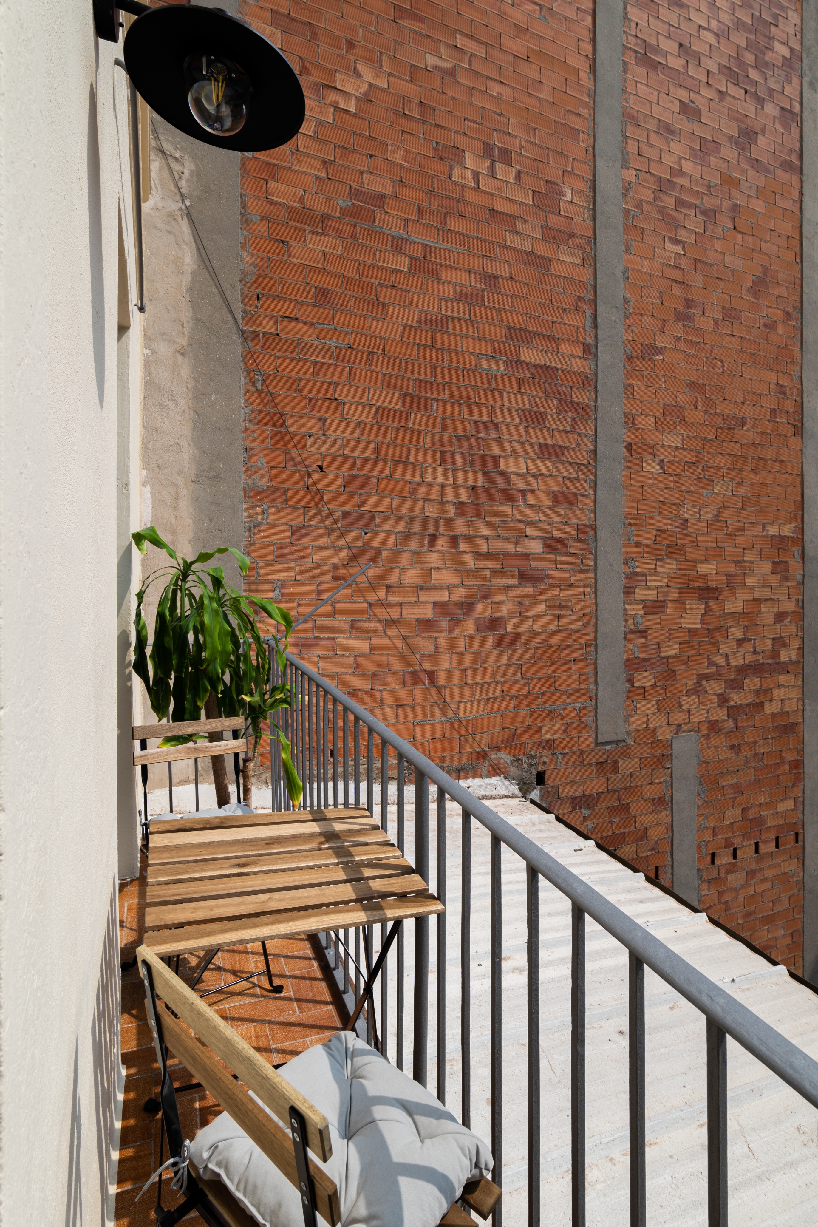 Balcony with a small wooden table, two wooden chairs, a potted plant, and a view of a brick wall
