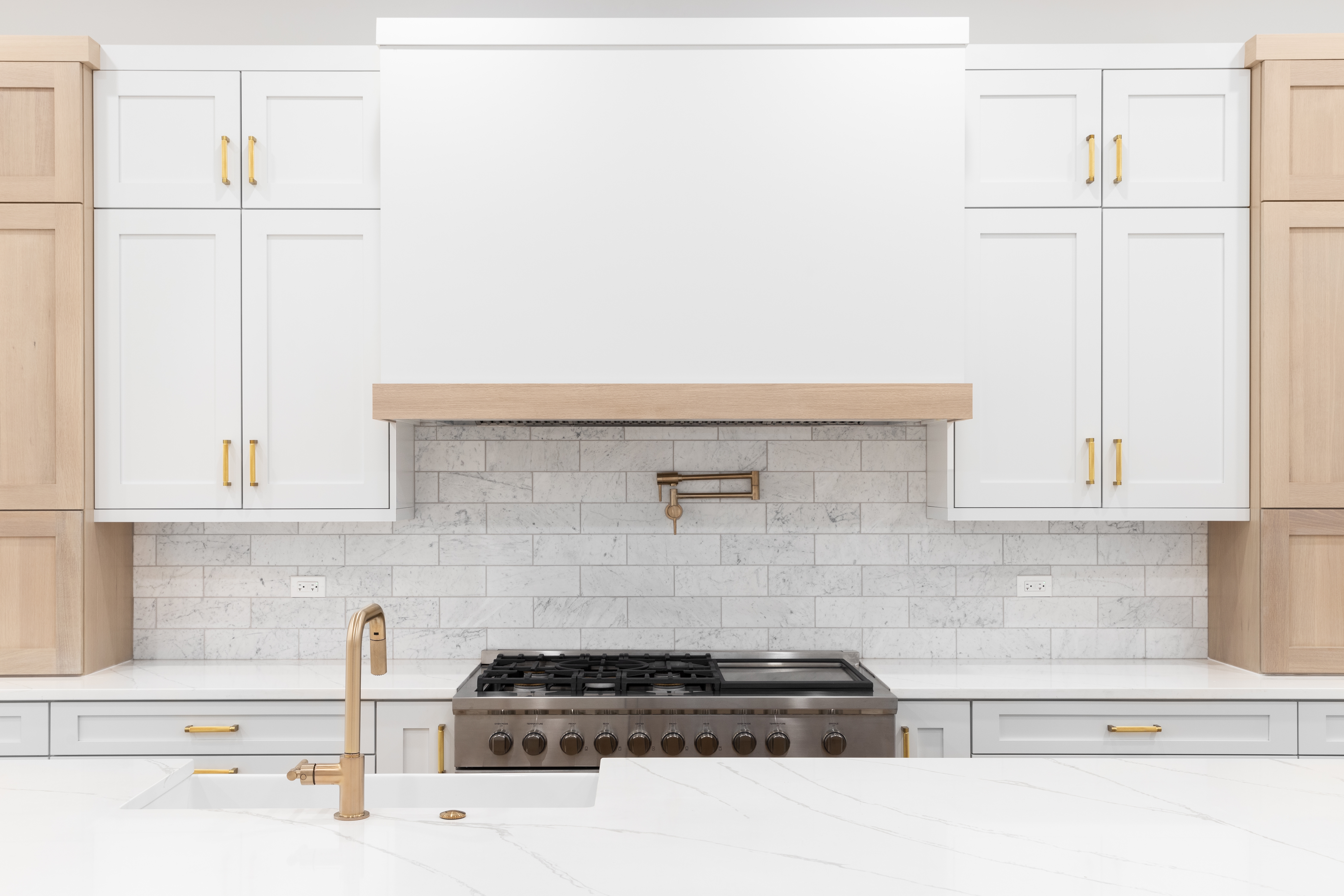Modern kitchen with white cabinetry, marble backsplash, gold fixtures, and a stainless steel oven