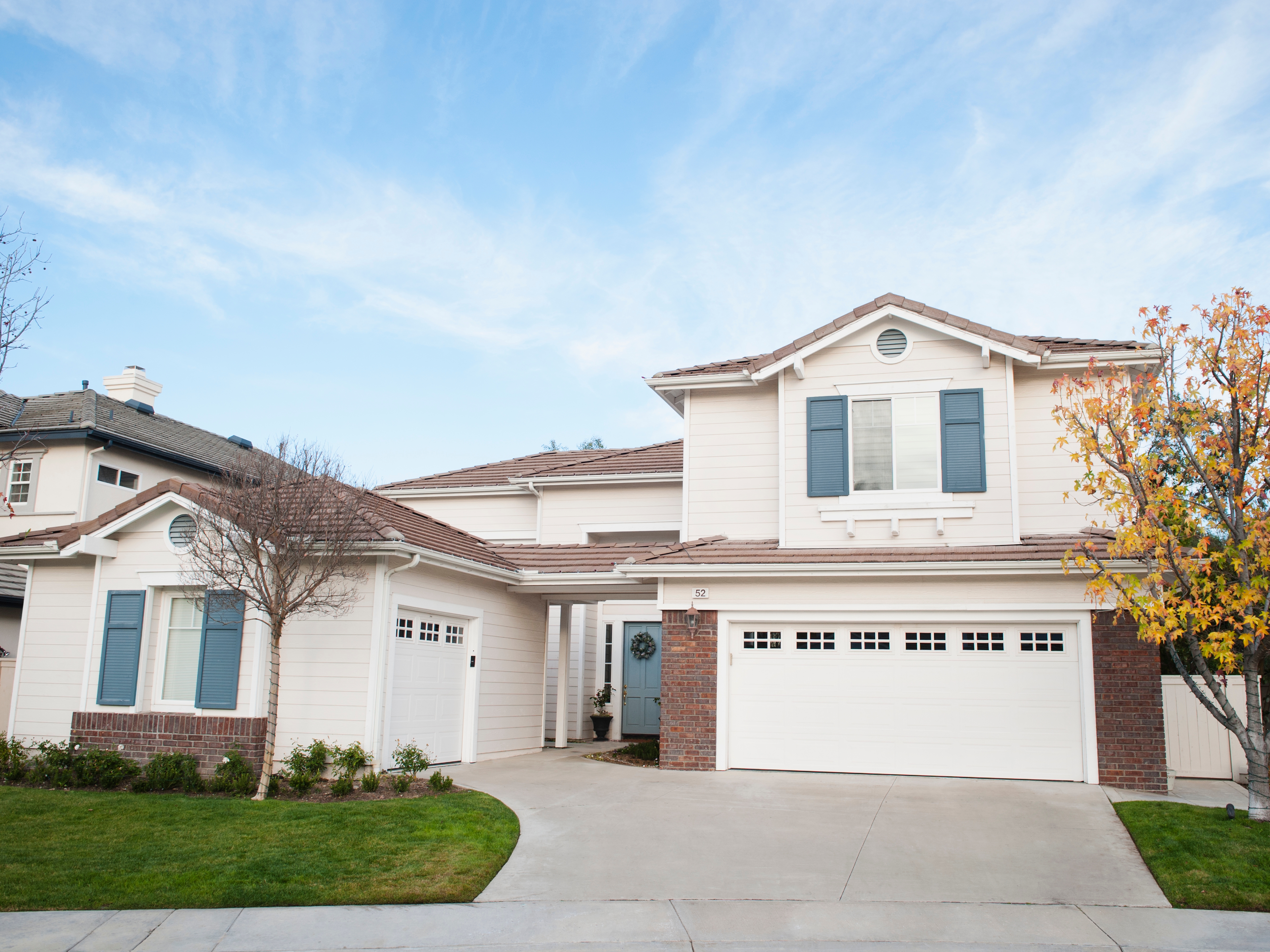 A modern, two-story suburban house with a three-car garage, brick accents, and surrounding trees, set in a tidy neighborhood
