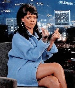 Rihanna makes a playful gesture during an interview on a cityscape-lit set