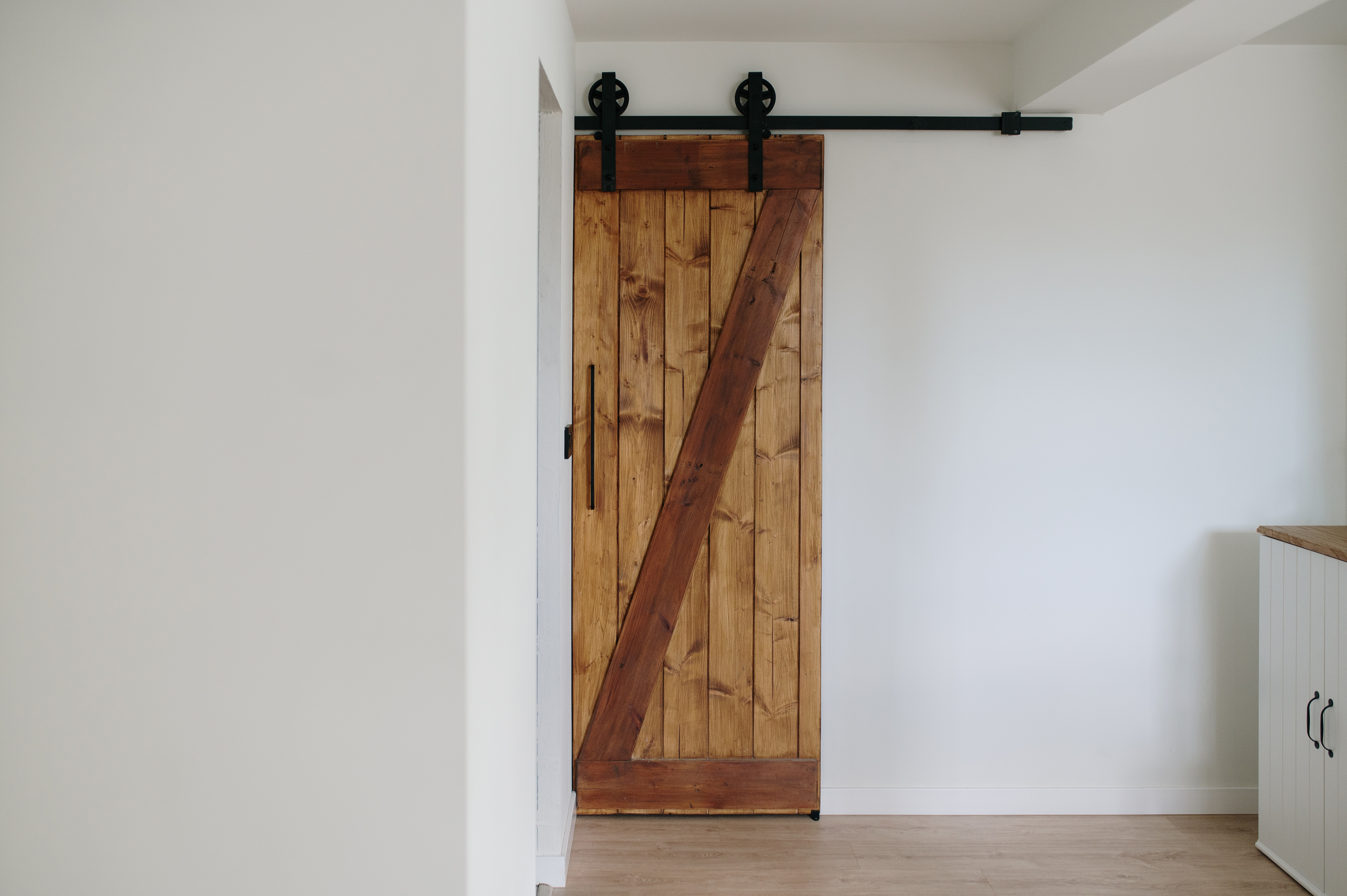 Wooden sliding barn door in a modern, minimalist room with white walls and light wooden floor