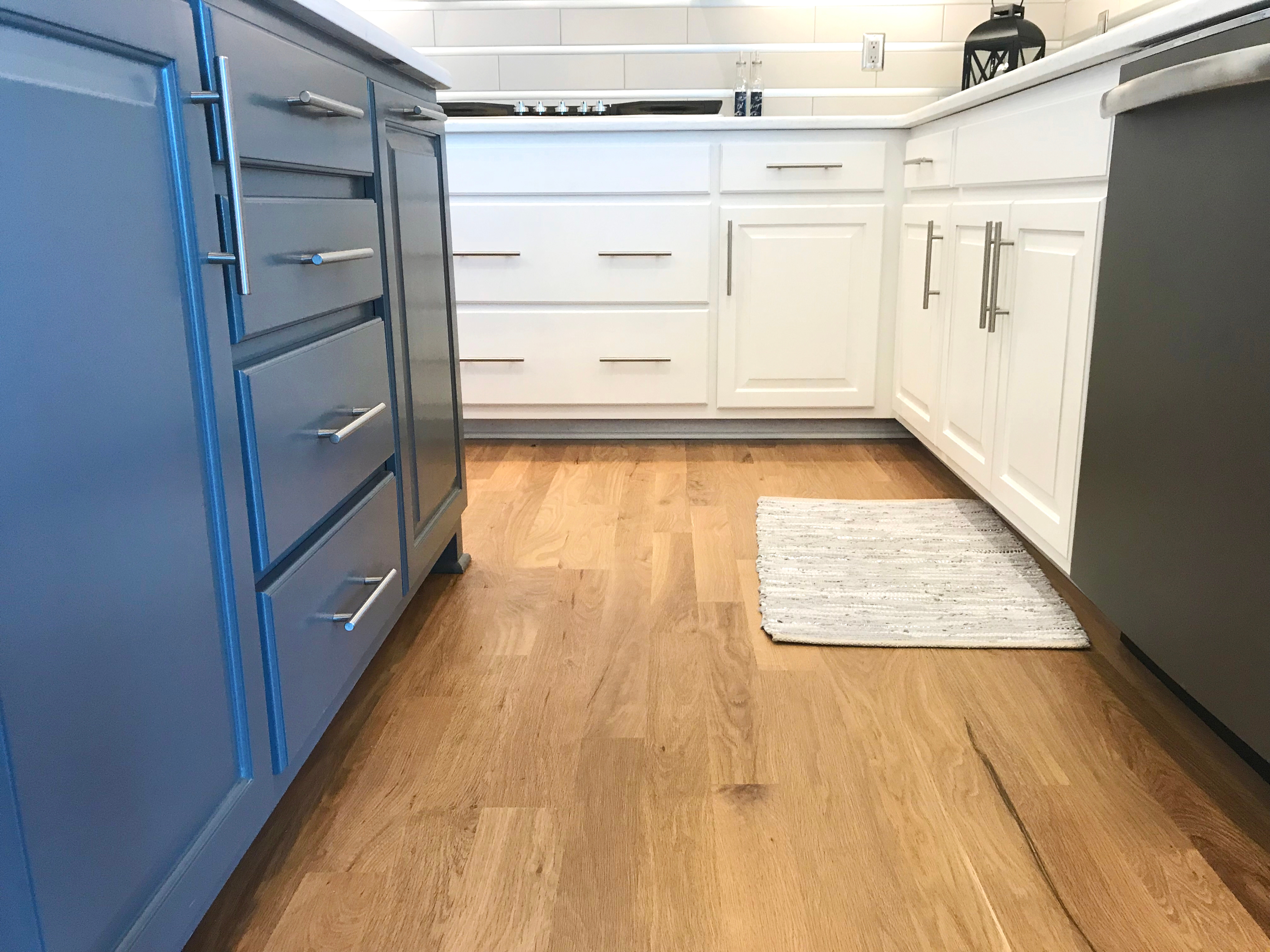 Modern kitchen with blue cabinets on one side, white cabinets on the other, wood flooring, and a small rug near the stove