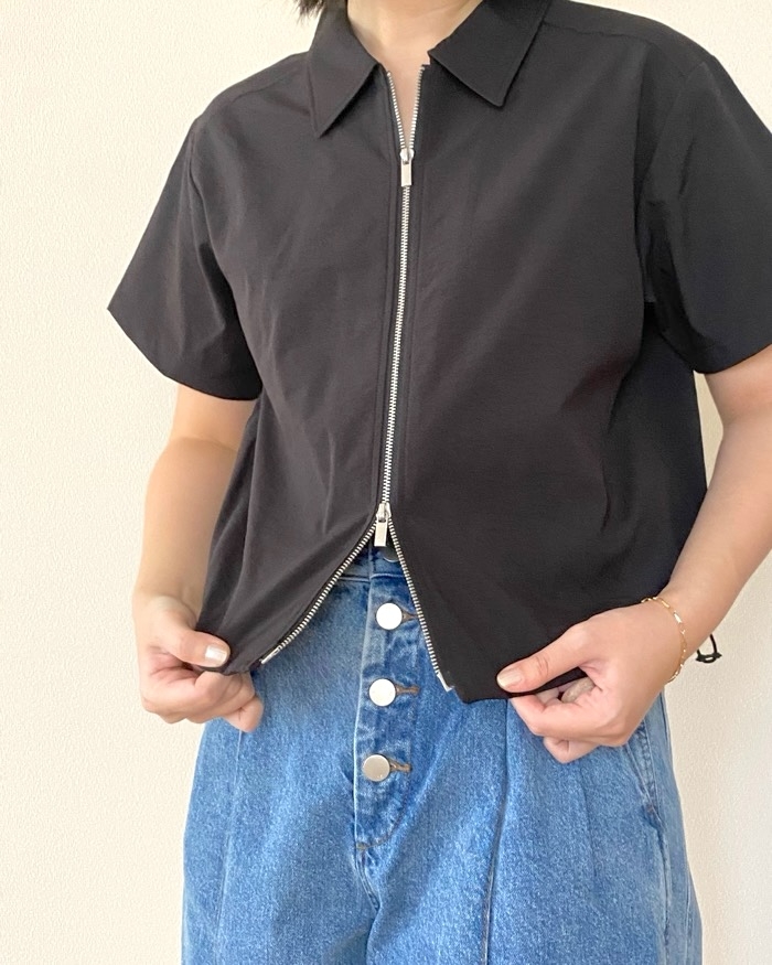 Person wearing a collared short-sleeve shirt with a front zipper, paired with high-waisted jeans with large buttons