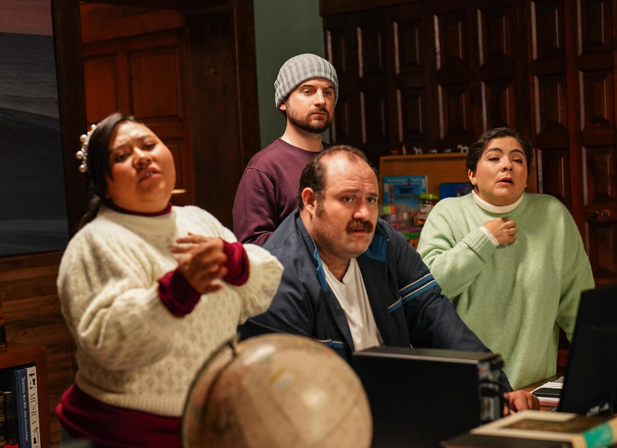 Cuatro personas viendo algo intrigante en una pantalla, vestidas de manera casual con suéteres, en un ambiente interior acogedor