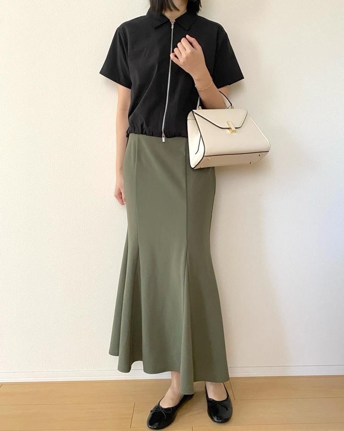 Person wearing a short-sleeve top and a long skirt, holding a handbag
