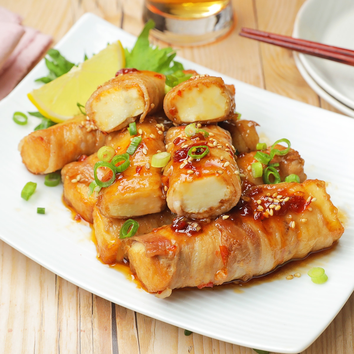 タレで味付けされた肉巻きチーズの盛り合わせ。添えられたレモンと刻んだネギが飾りとして配置されています。