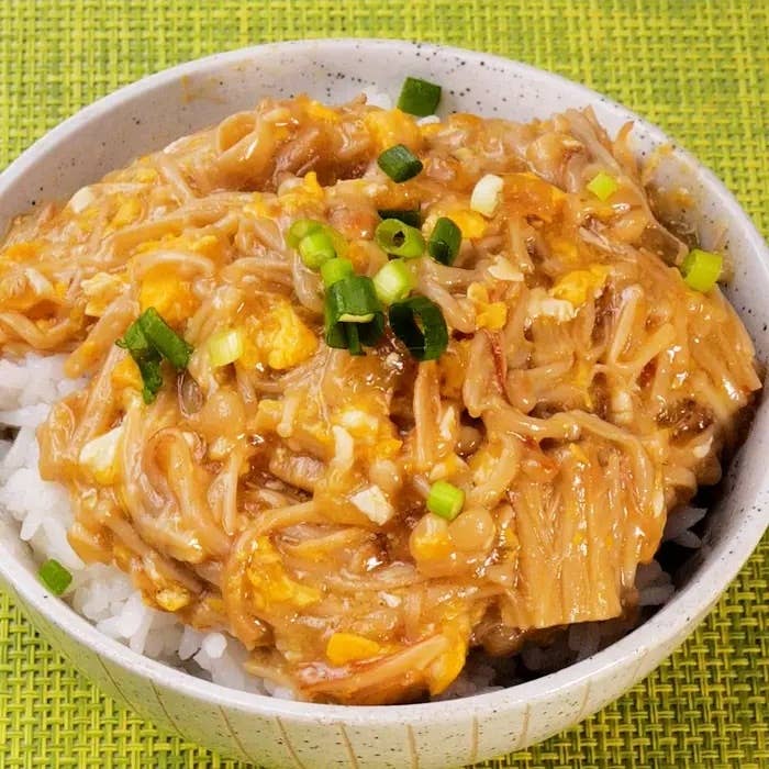 どんぶりに盛られた卵とエノキがのったご飯。ネギがトッピングされ、家庭的な料理の一例。