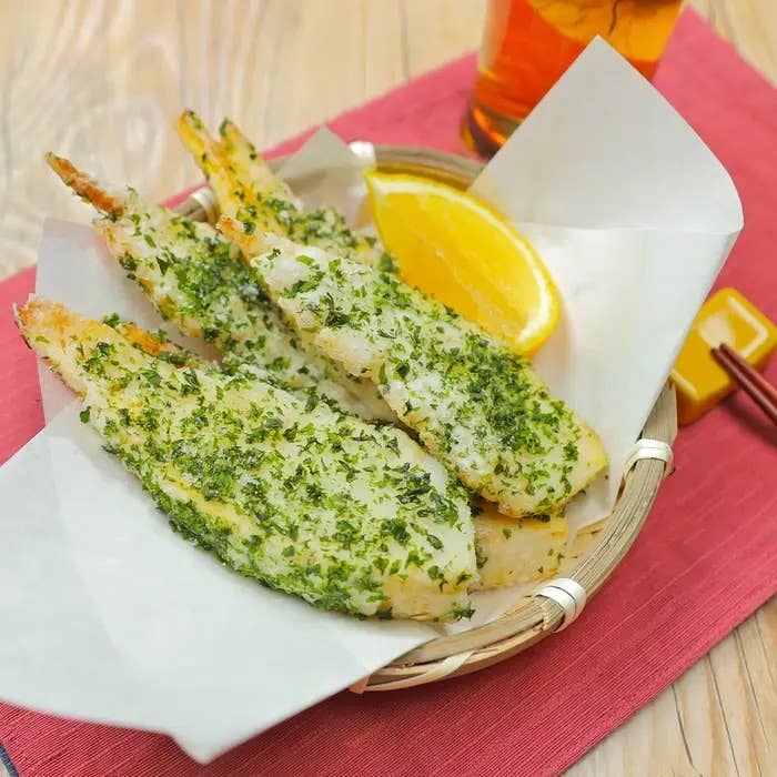 カゴに盛られたハーブで覆われたエビの揚げ物とレモンスライスが添えられた料理。
