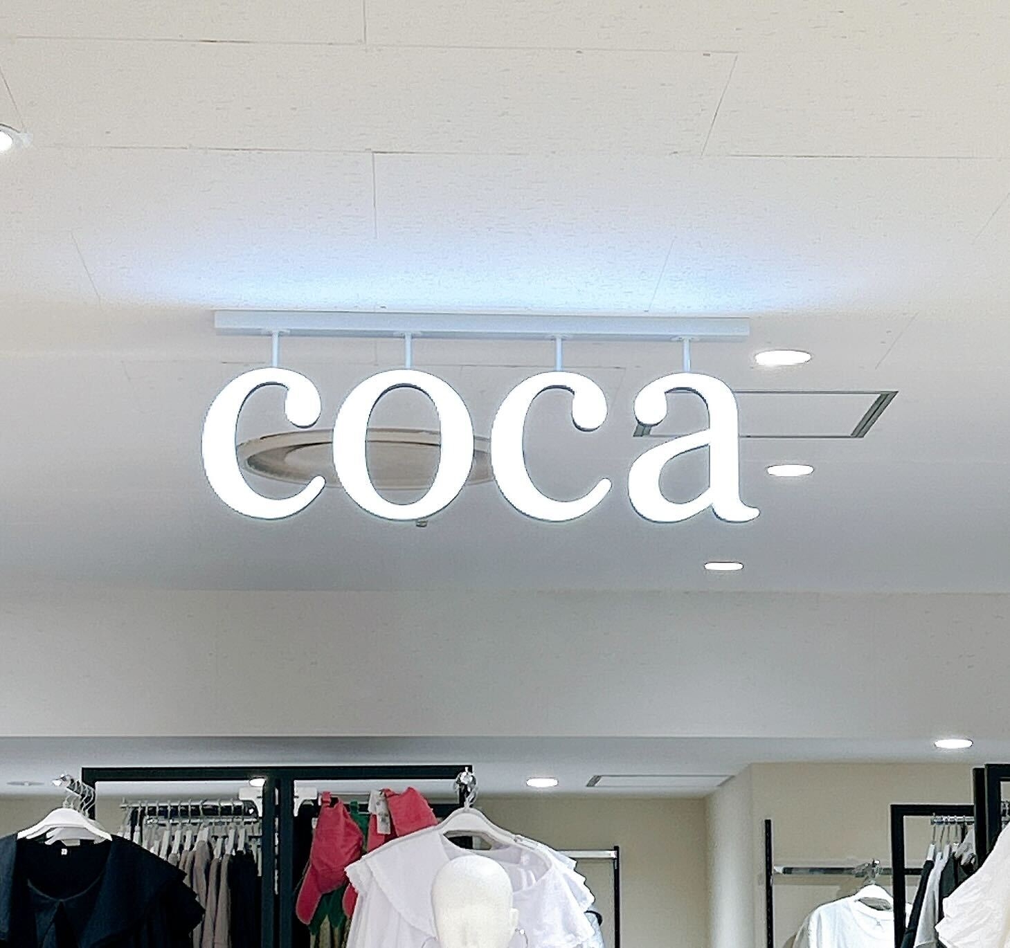 店内に「coca」の電光サインがあり、衣類が背景に見える。