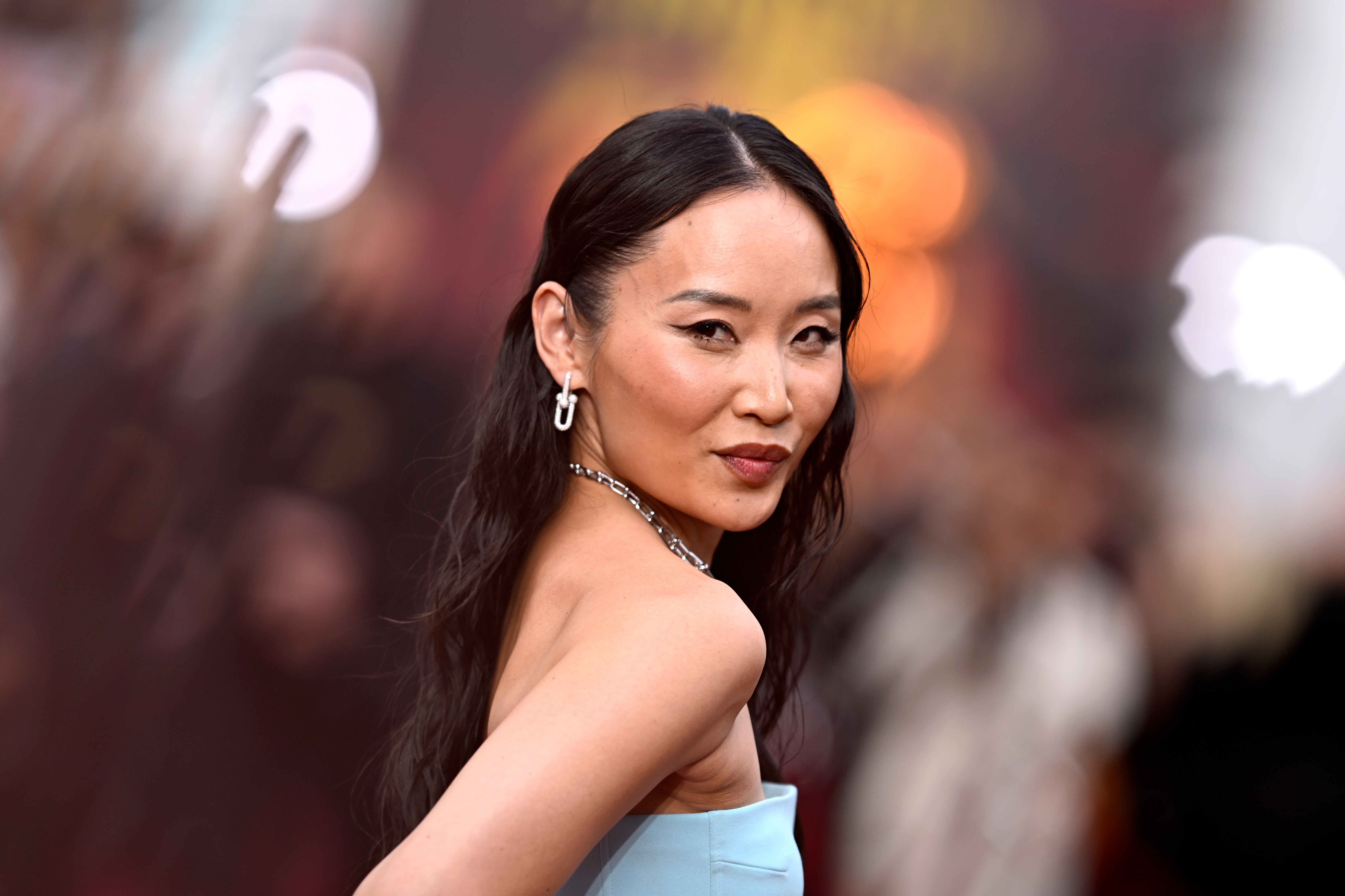 A woman in an elegant strapless gown poses confidently on the red carpet, with long hair and chandelier earrings