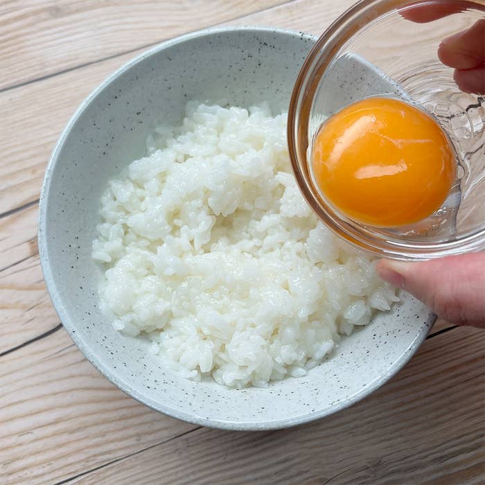 白いご飯の上に卵黄がのせられようとしている場面。