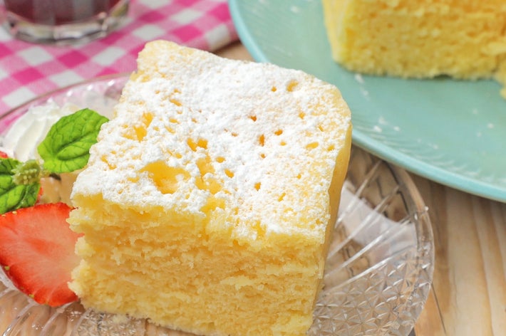 ケーキの一切れが透明な皿にのり、横にはイチゴとミント。背景には別の皿に同じケーキ。