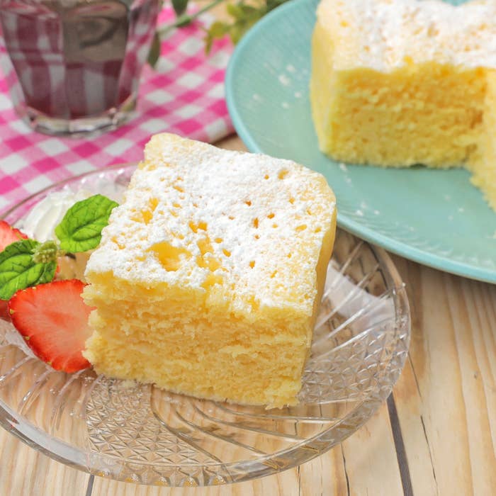 ケーキの一切れが透明な皿にのり、横にはイチゴとミント。背景には別の皿に同じケーキ。