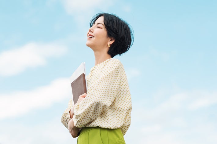 女性が屋外で文書を抱えて笑顔で立っている。