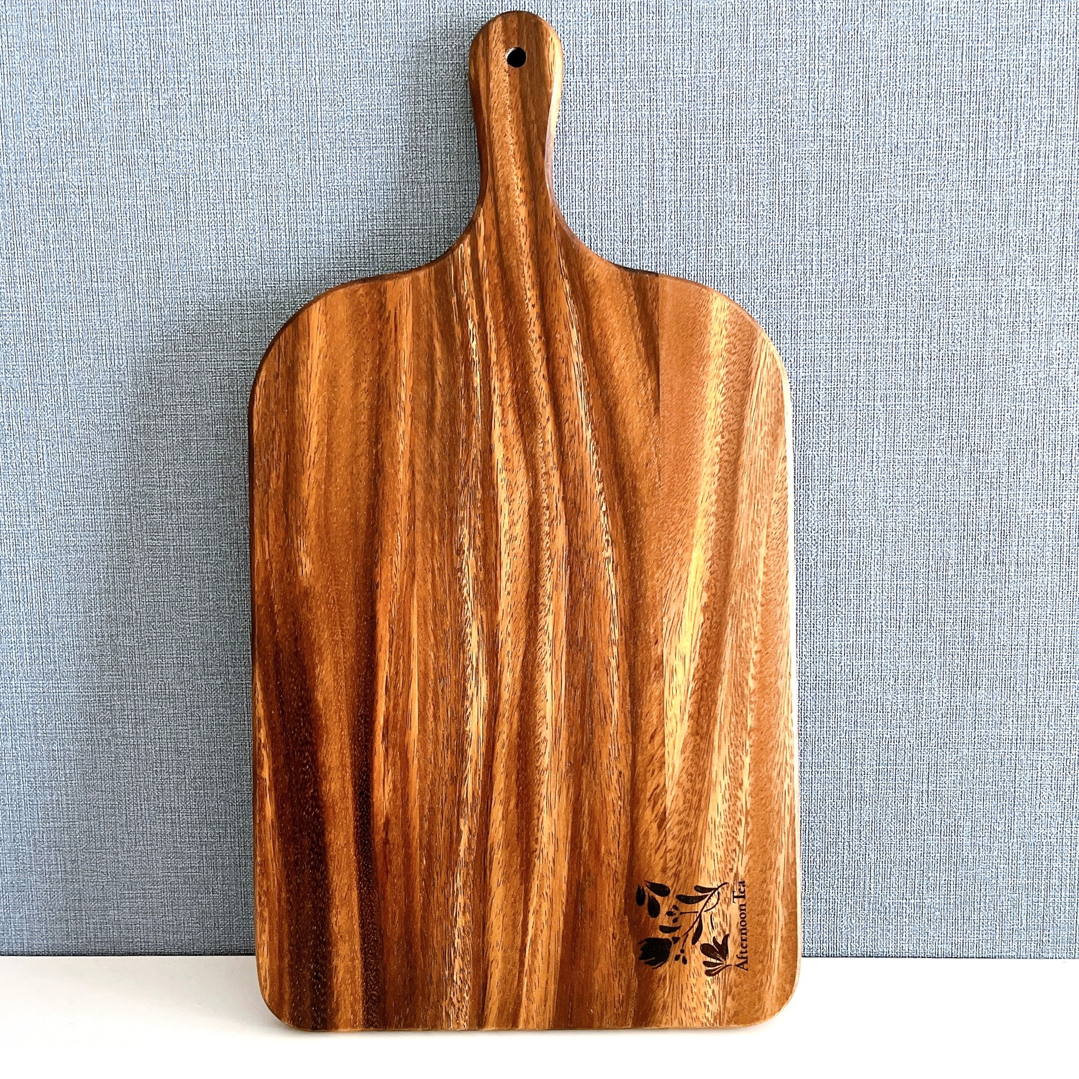 木製のカッティングボードが垂直に立てかけられている。表面に木目が美しく、下部に模様がある。