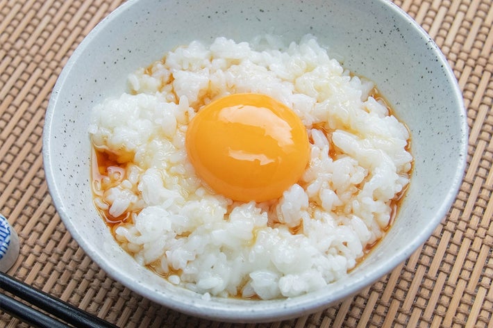 卵かけご飯が入った茶わん。生卵としょうゆがご飯の上にかかっている。横には箸が置かれている。