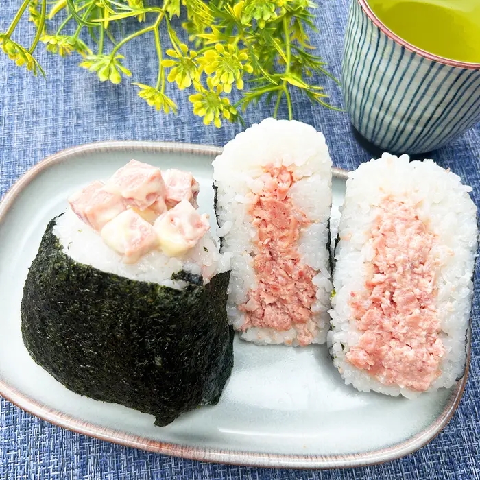 皿に盛られた2つのポークランチョンミートおにぎり。背景に飲み物と草がある。