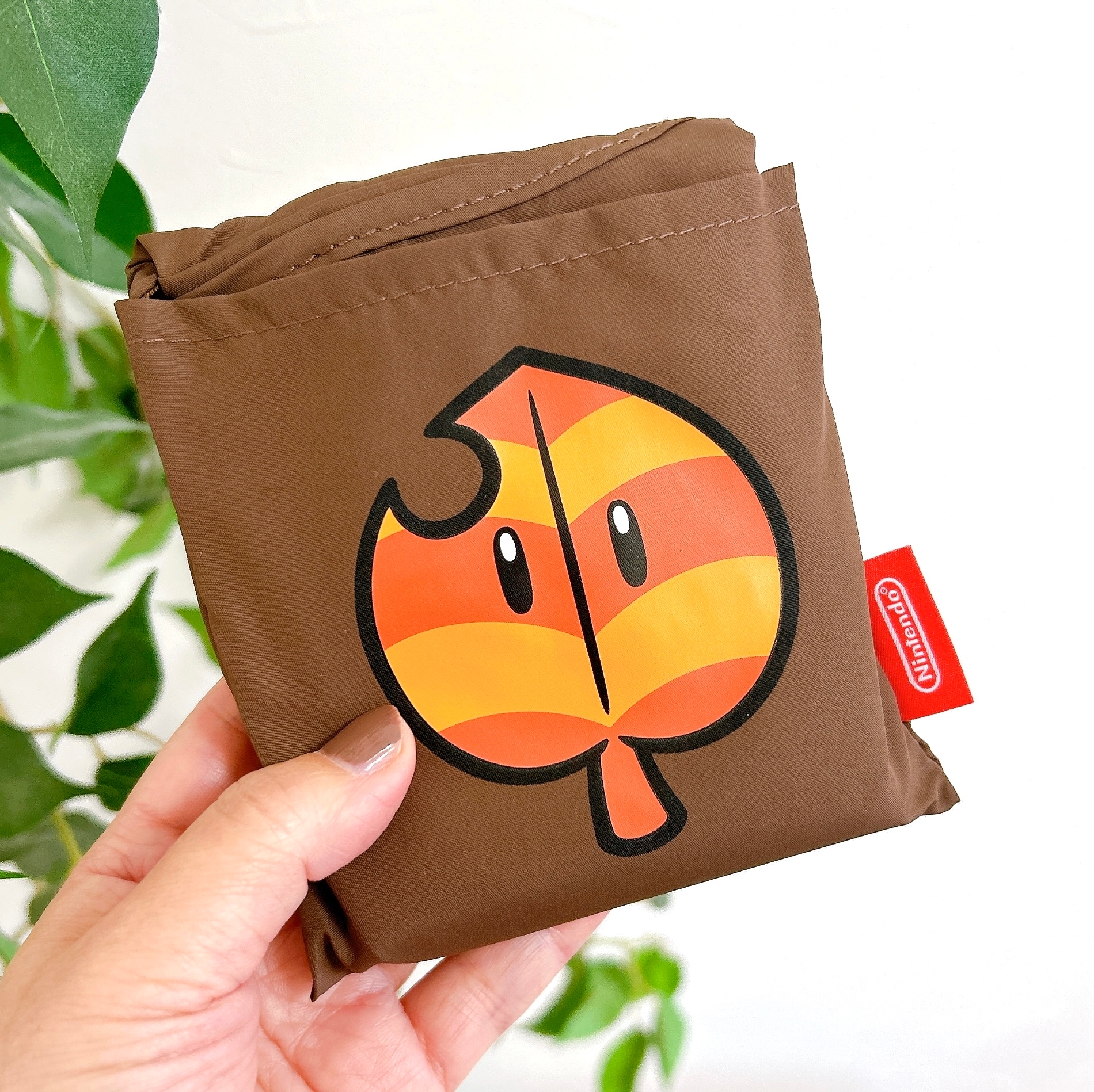 任天堂のマークがついた葉のイラストがあるバッグを手に持っている。