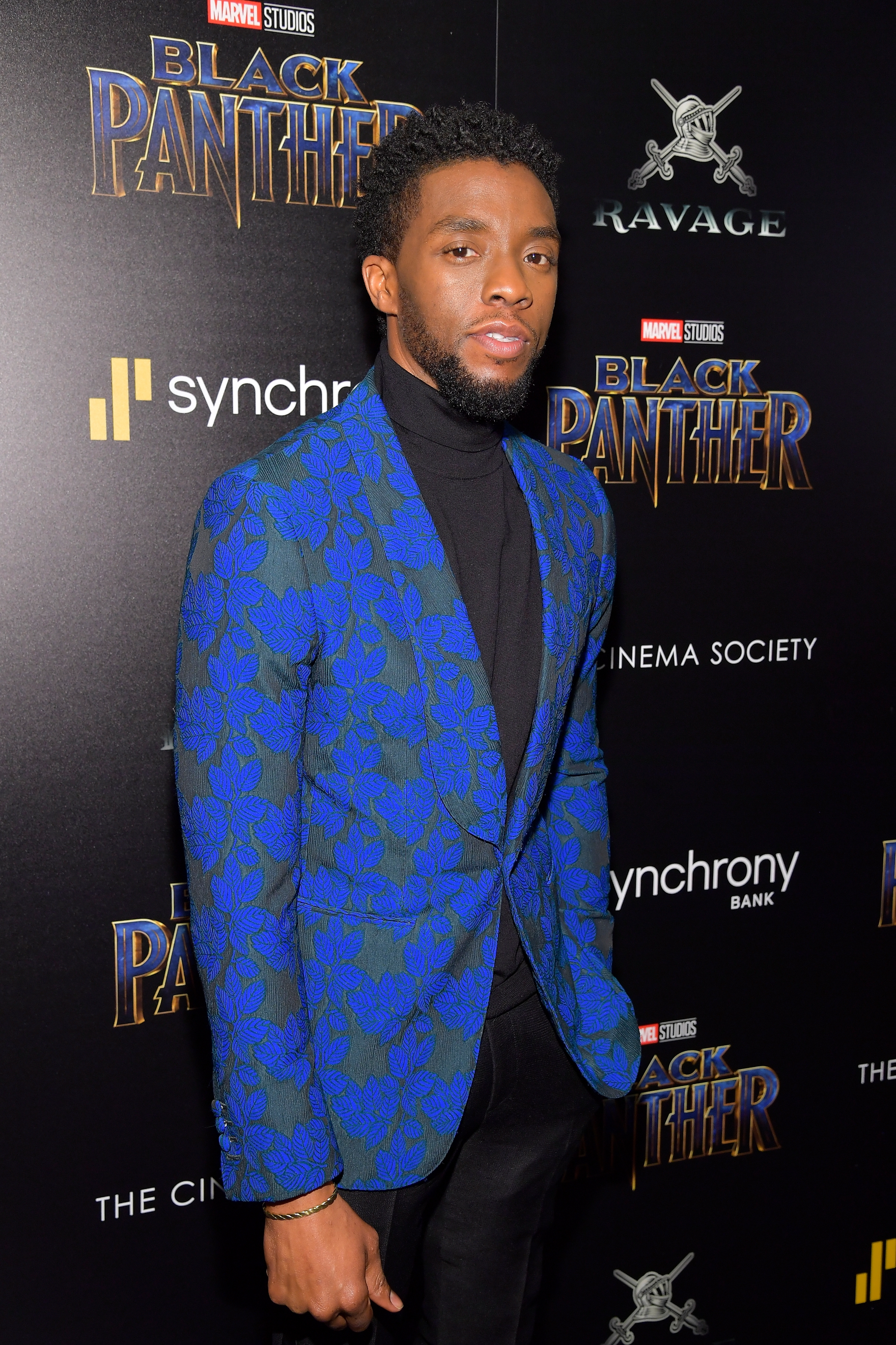 Actor on red carpet wearing a stylish patterned blazer over a turtleneck at a "Black Panther" event backdrop