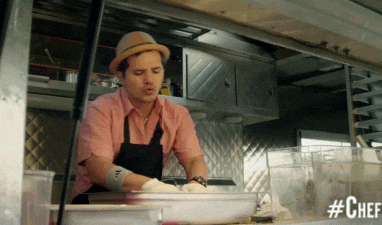 Chef in a food truck enthusiastically preparing a dish, wearing a hat and apron, with #ChefMovie text on screen