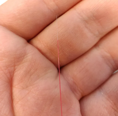 A close-up of a hand holding a single strand of red thread between fingers