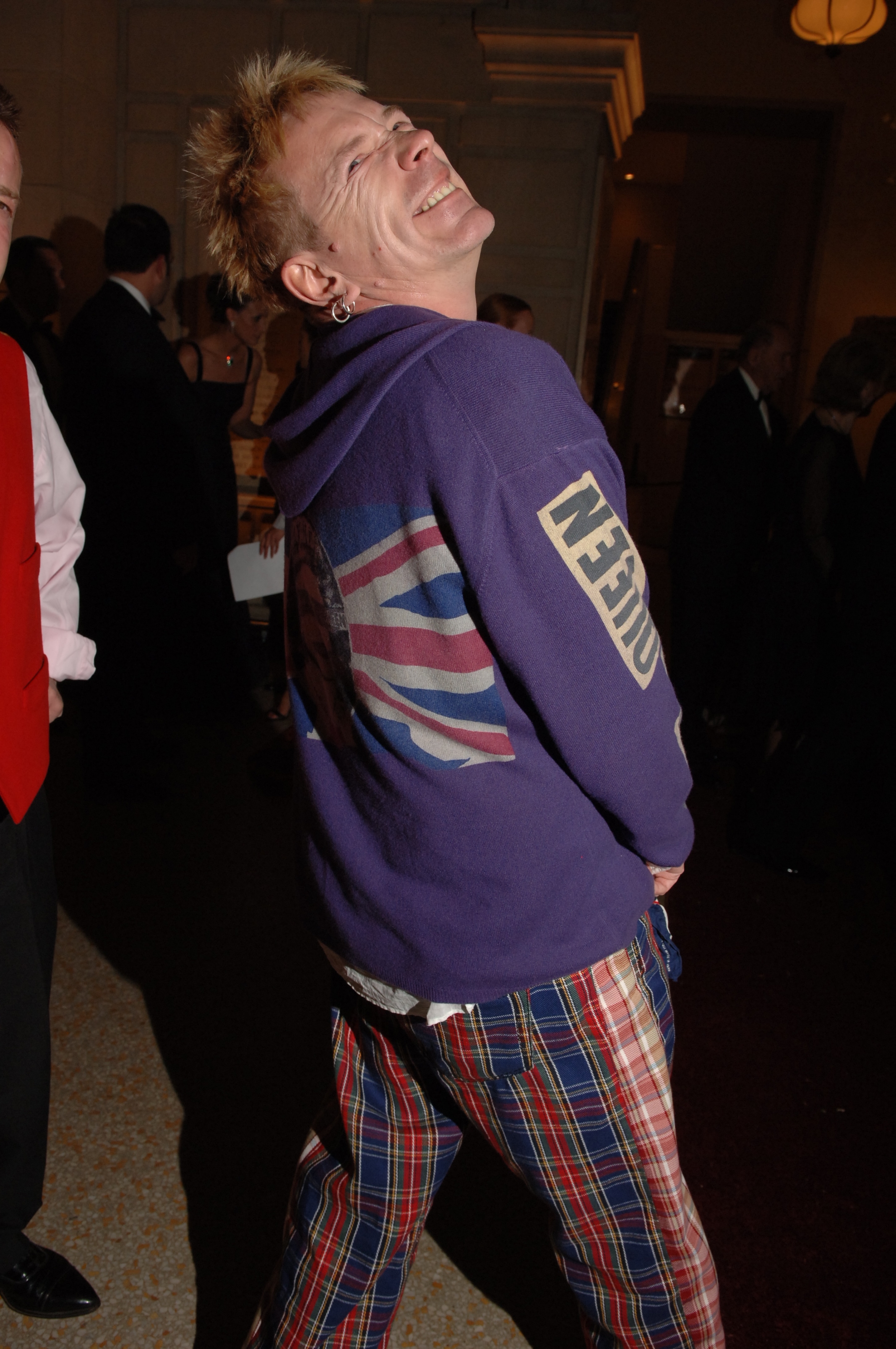 Person playfully posing, wearing a hoodie with bold text on the back and plaid pants, in a lively event setting