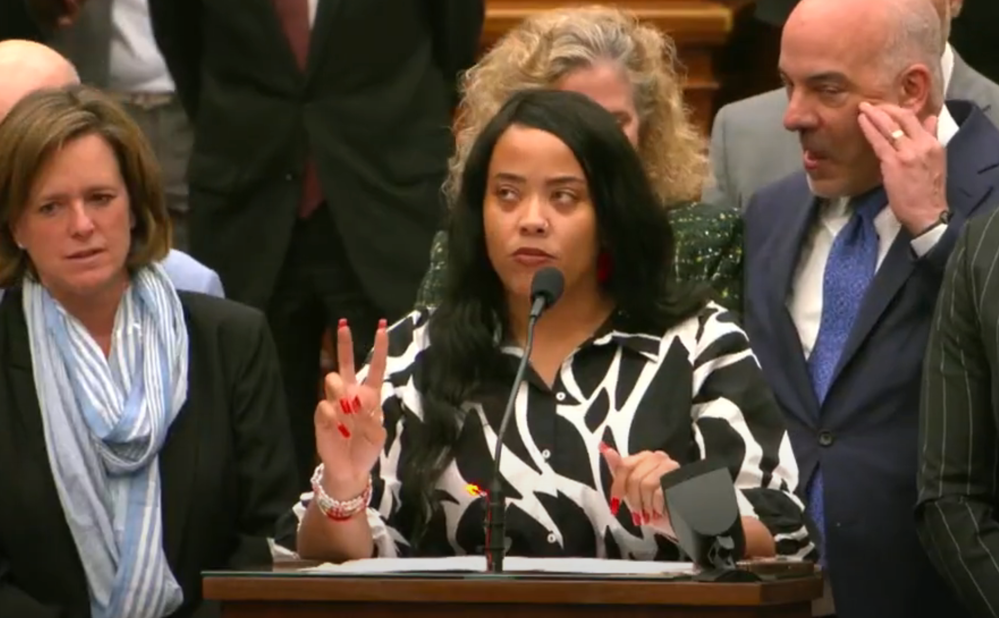 A person speaks at a podium during a formal event. They are surrounded by people in business attire