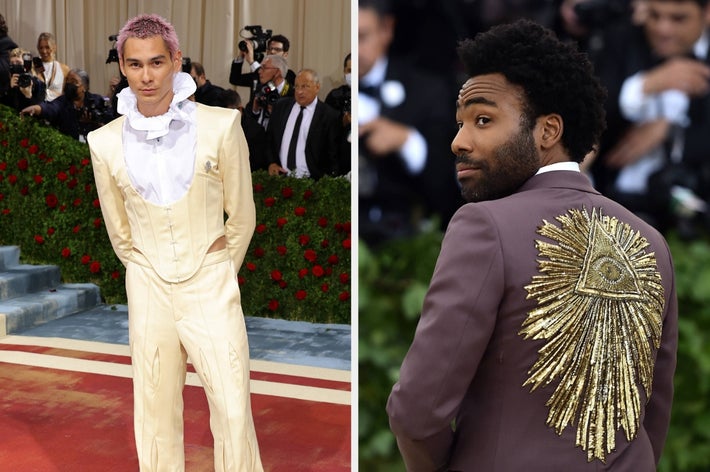 Two individuals at a formal event: One in a cream ruffled suit, the other in a brown suit with a gold sunburst design on the back