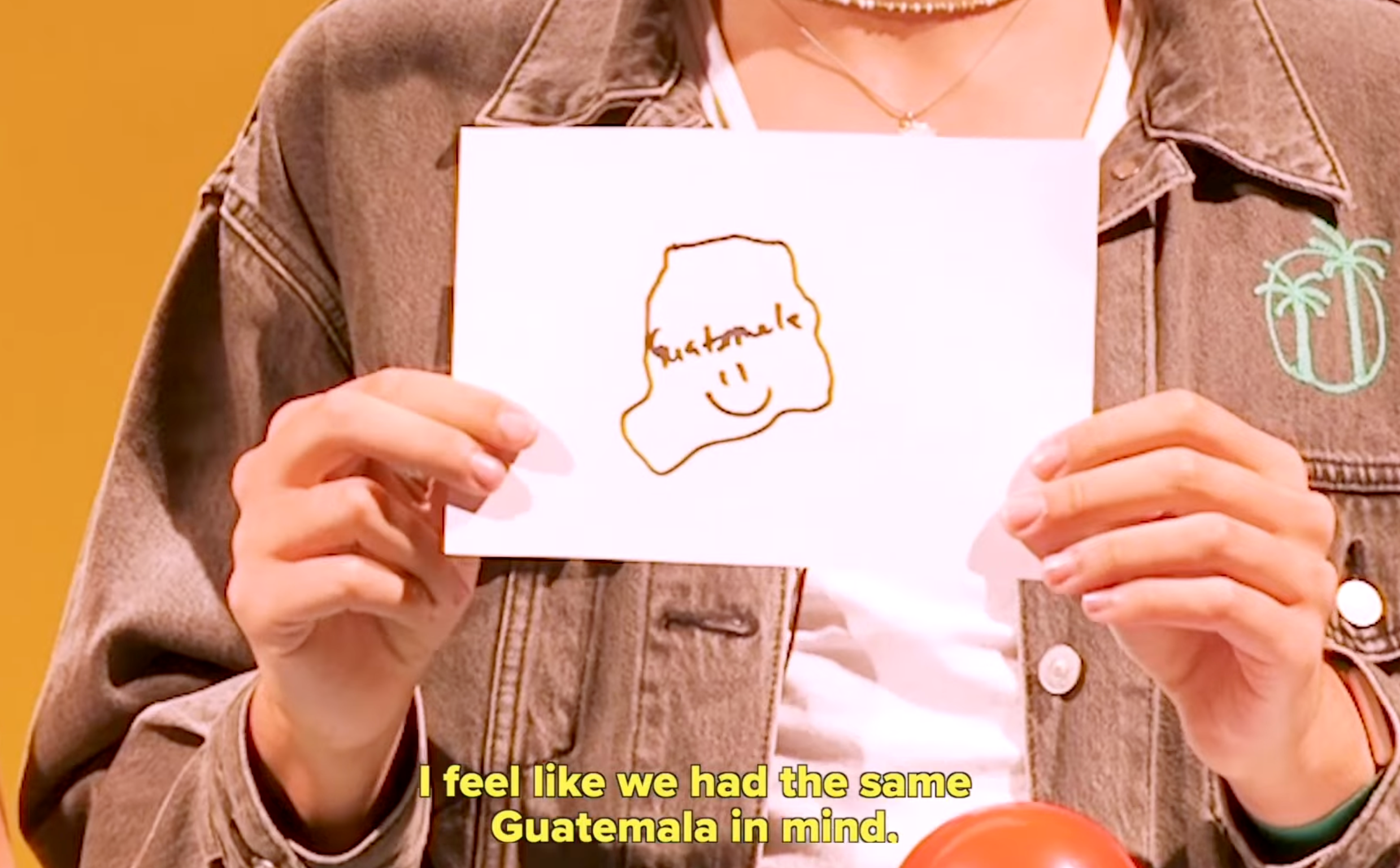 Person holding a paper with a simple map drawing labeled "Sustainable" and a smiley face. Caption reads: "I feel like we had the same Guatemala in mind."