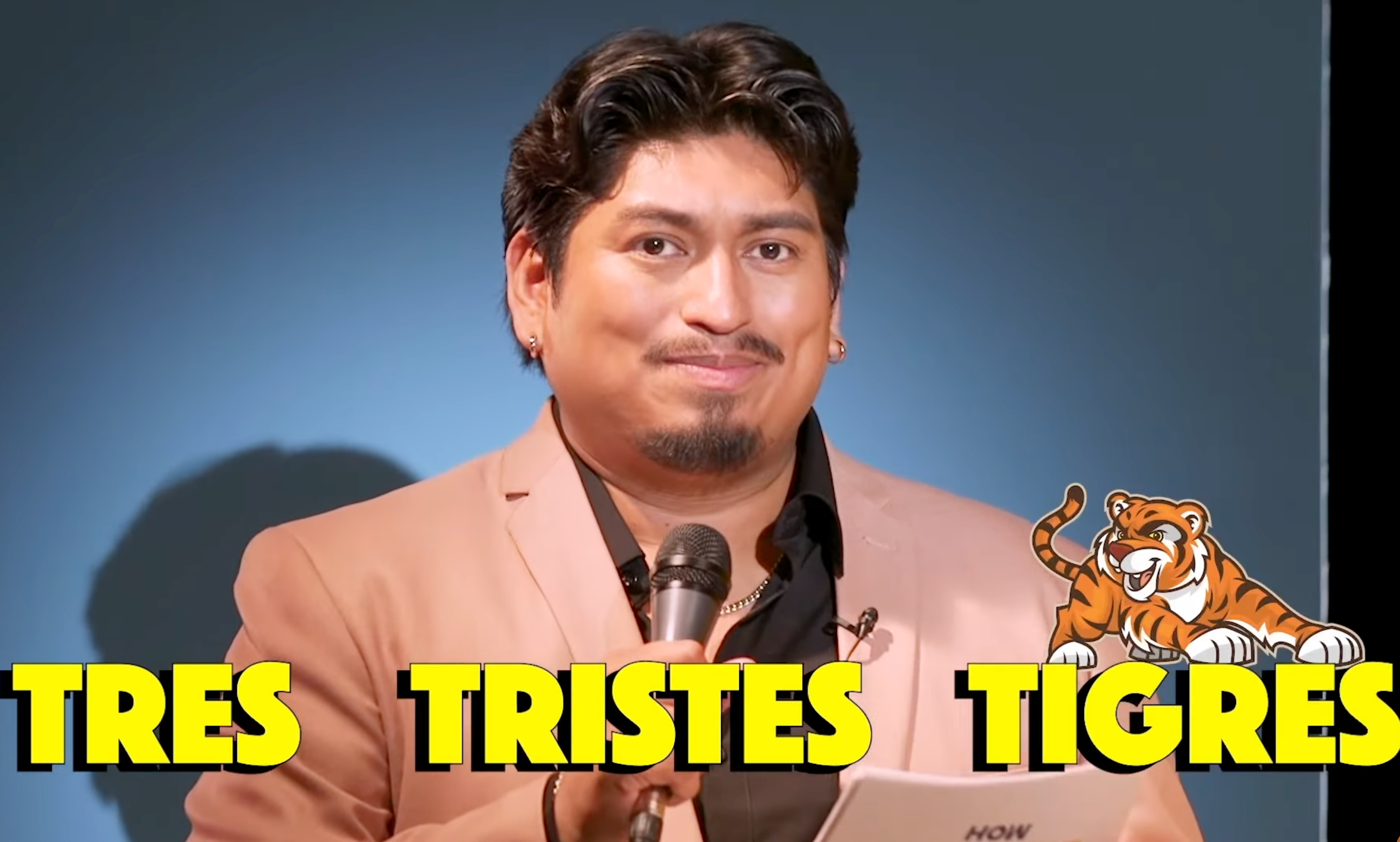 Person in a suit holding a microphone, with large text reading "Tres Tristes Tigres" next to a cartoon tiger illustration