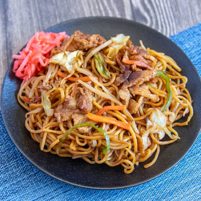 皿に盛られた焼きそばには、キャベツ、にんじん、肉がトッピングされており、添えられた紅しょうがが見える。