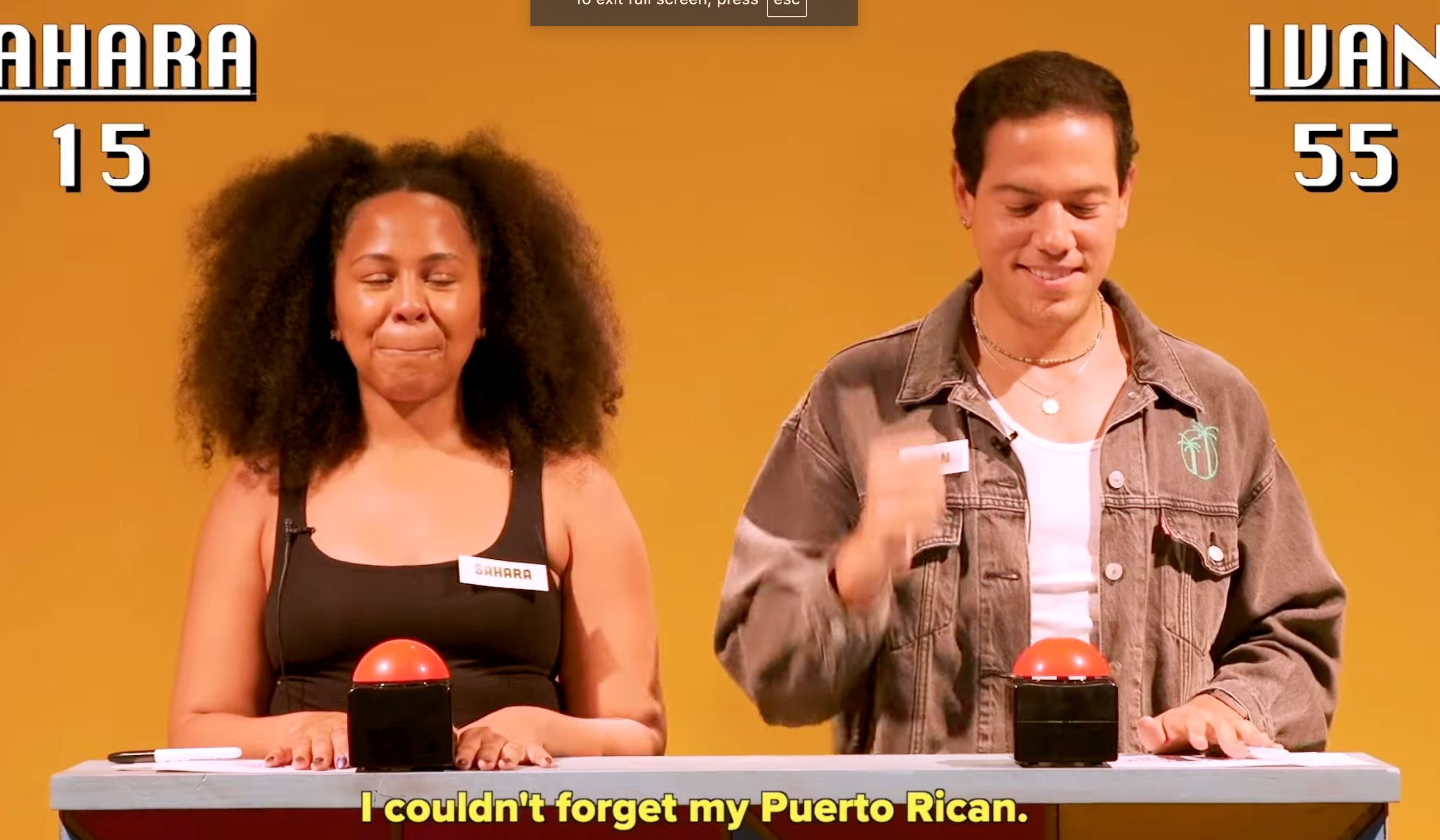 Two people at a game show podium with buzzers. Scoreboard reads: Zahara 15, Ivan 55. Caption: "I couldn't forget my Puerto Rican."