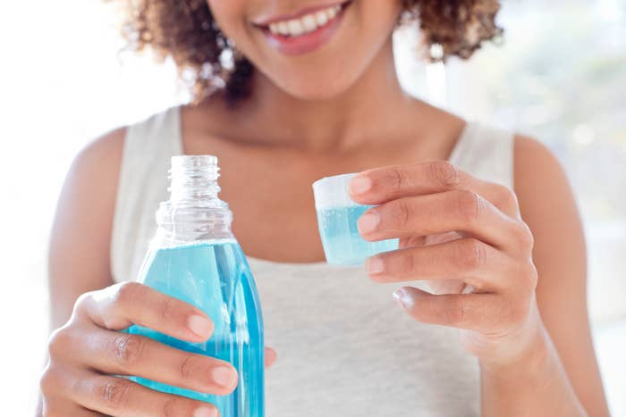 A person smiles while pouring mouthwash into a cap, suggesting a focus on dental hygiene and self-care