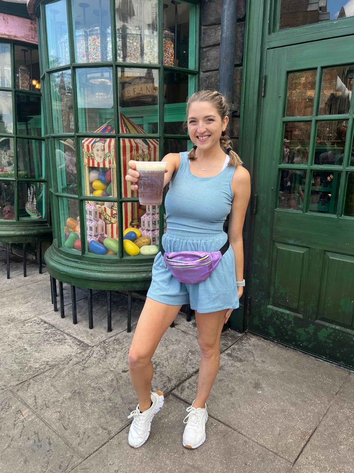 Person successful  a casual bluish  outfit holding a drink, smiling successful  beforehand   of a storefront with colorful candy jars