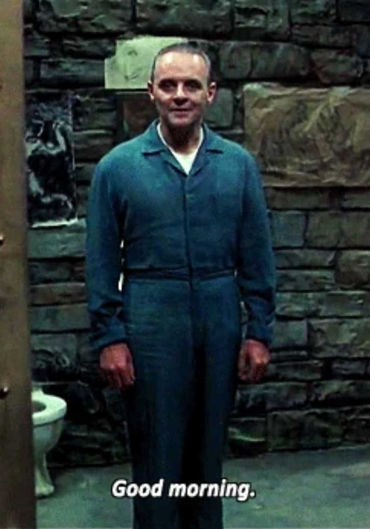 Man in a prison jumpsuit stands in a cell, smiling slightly. Subtitles: "Good morning."