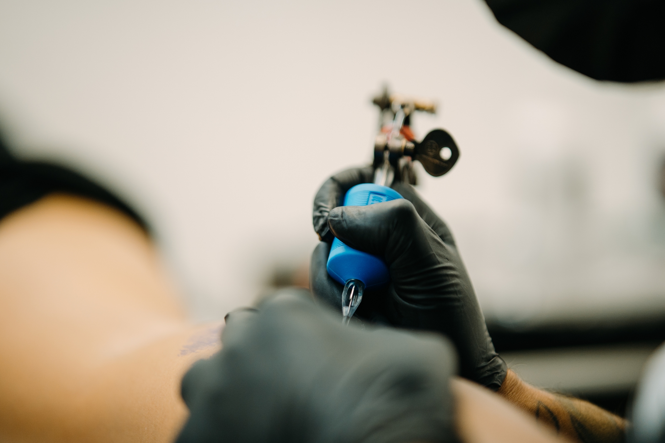 Person wearing gloves using a tattoo machine on someone's skin, suggesting a professional tattooing process