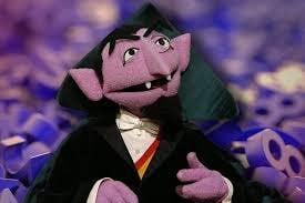 Un personaje de marioneta con colmillos vistiendo un traje con capa, en un escenario lleno de números en el fondo