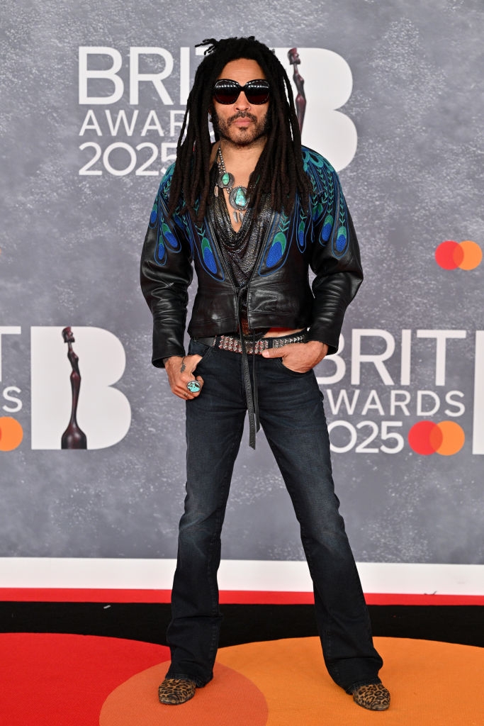 Person in a leather jacket with intricate design and jeans at the Brit Awards 2025. They're wearing sunglasses and have long, styled hair