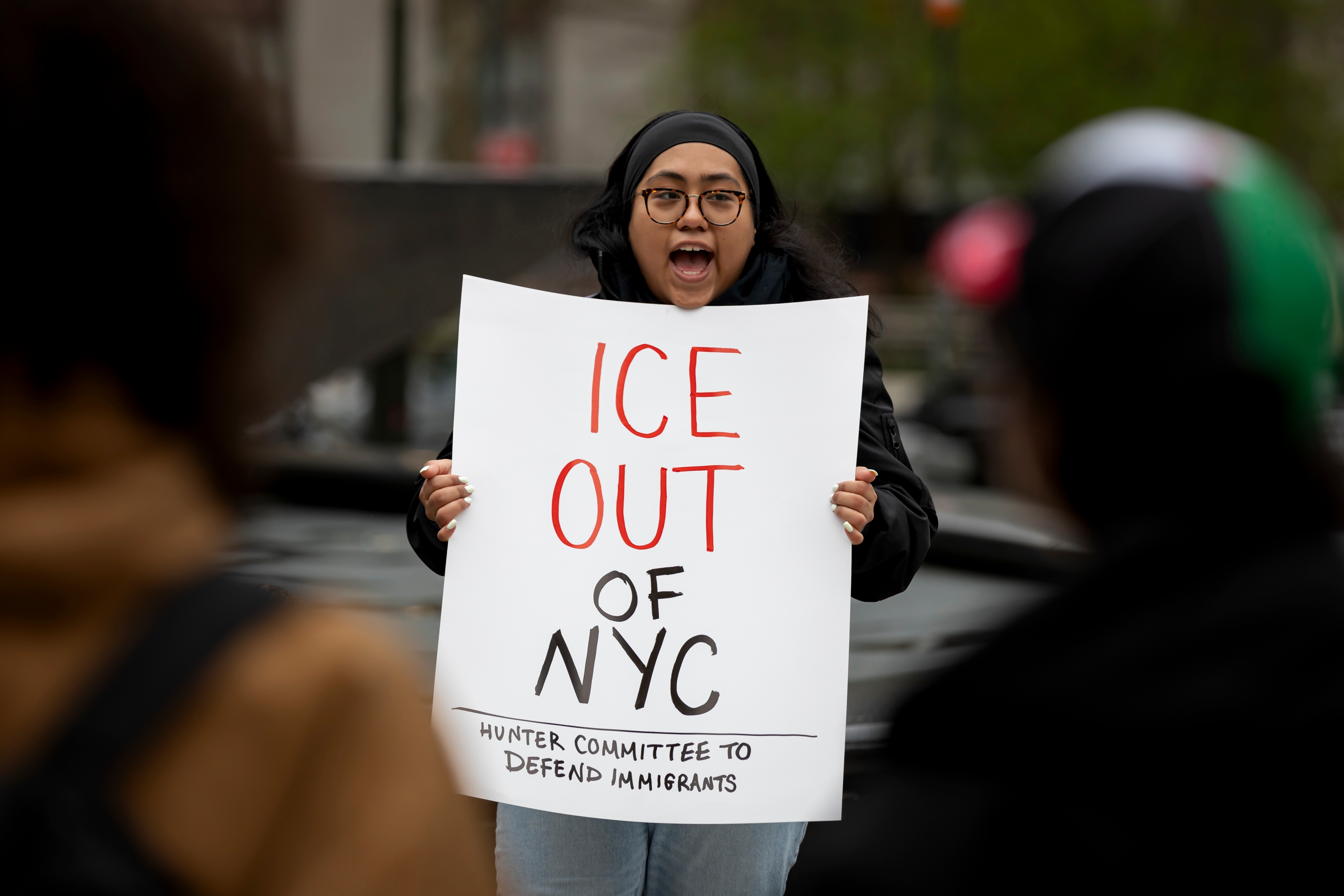 A person holds a sign reading &quot;ICE OUT OF NYC. Hunter Committee to Defend Immigrants&quot; during a public protest