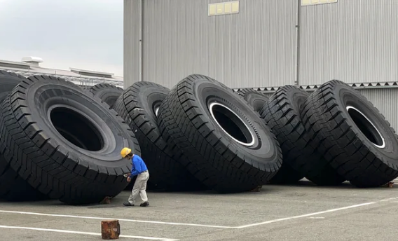 Person in hard hat standing next to giant industrial tires, aligned upright in a row outside a warehouse