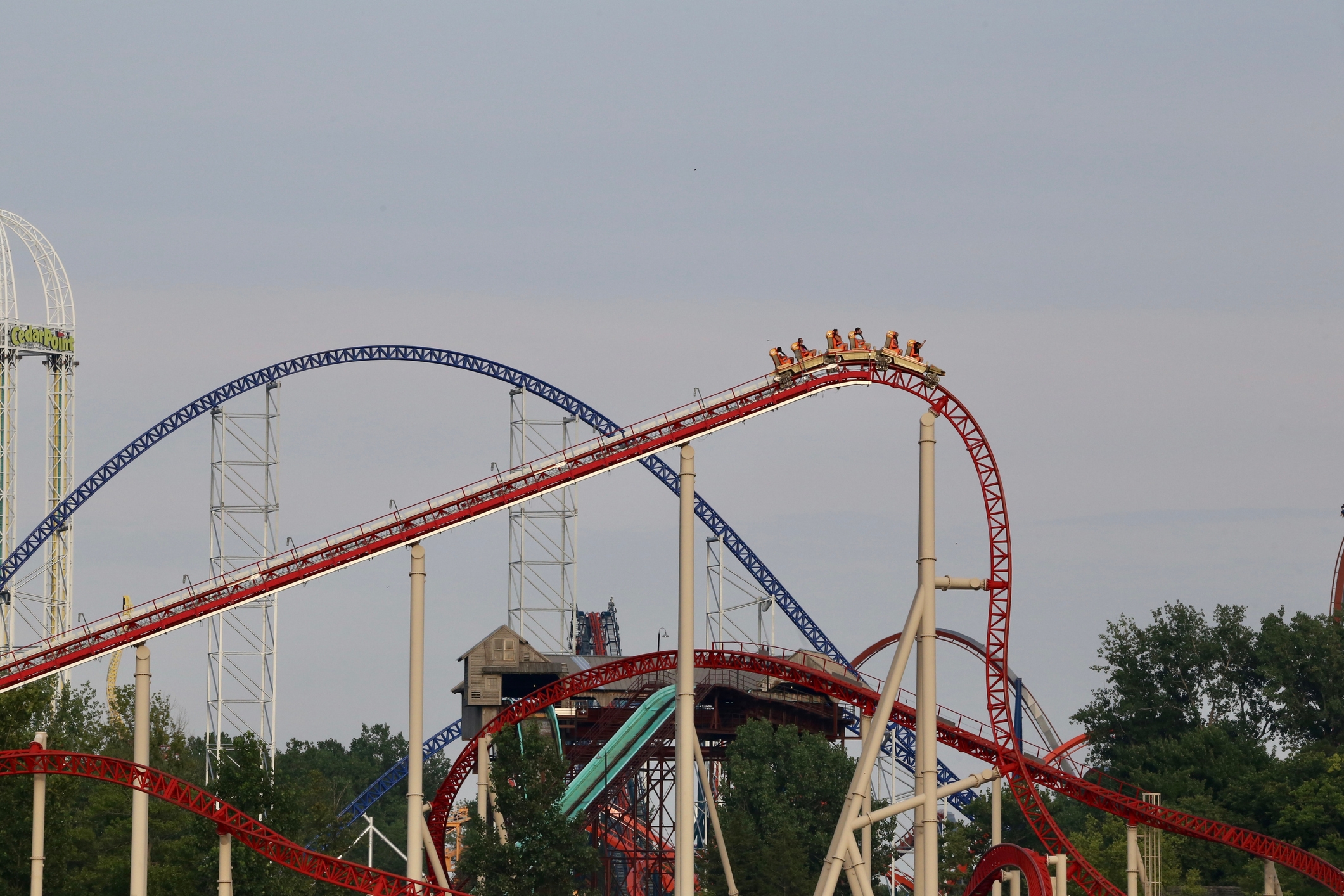 People riding a roller coaster at an amusement park, ascending a steep track with loops and turns visible in the background