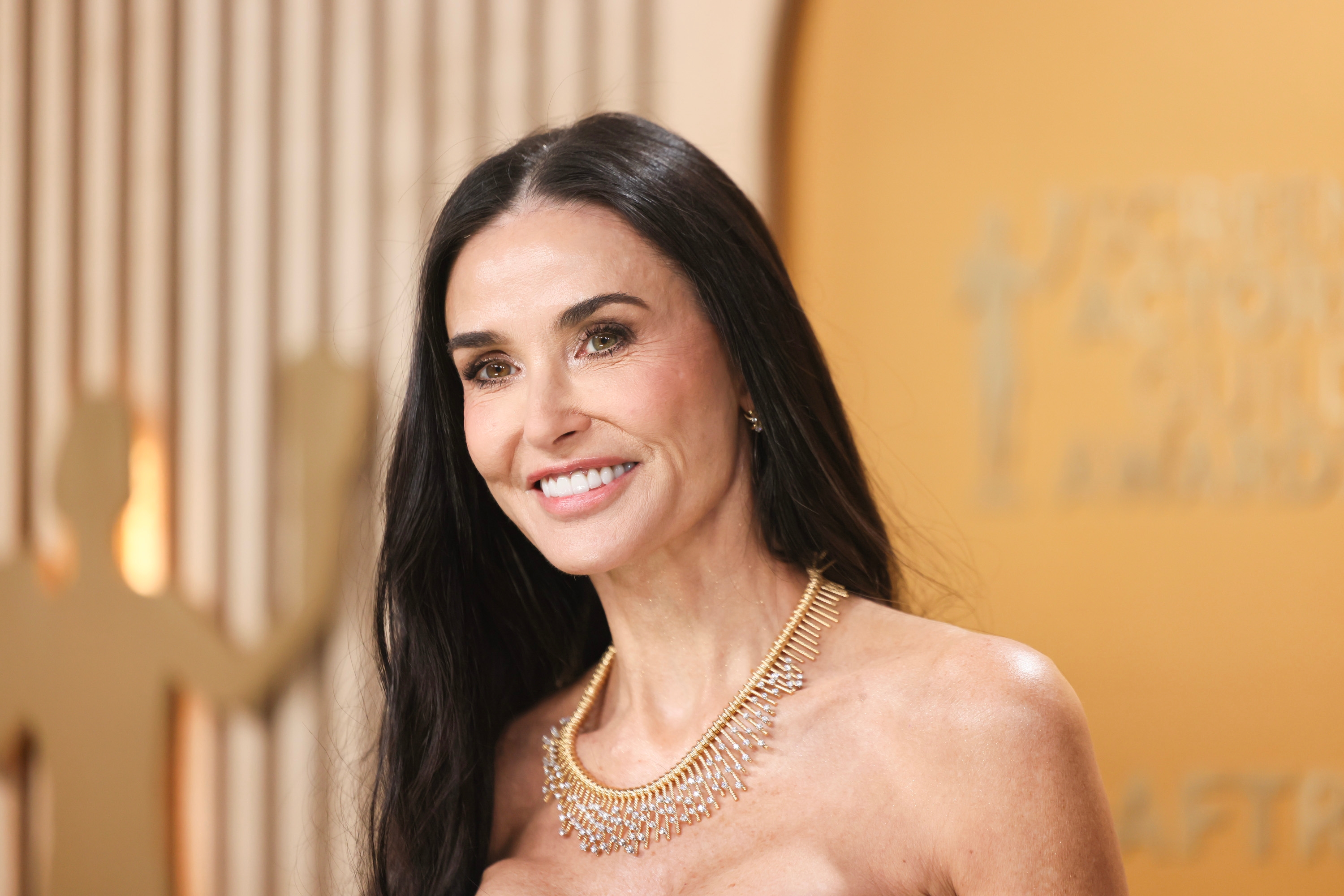 Woman smiling on the red carpet, wearing an elegant strapless outfit and a statement necklace