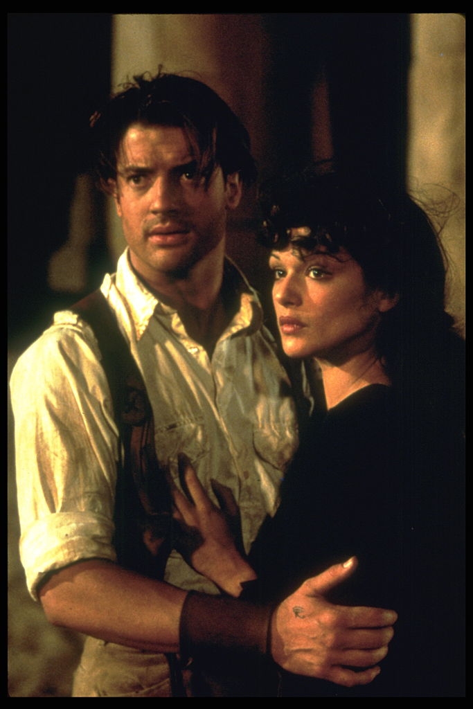 Two people in period-style clothing, looking into the distance. The man, Brendan Fraser wears a loose shirt, and the woman, Rachel Weisz has wavy hair, holding onto him
