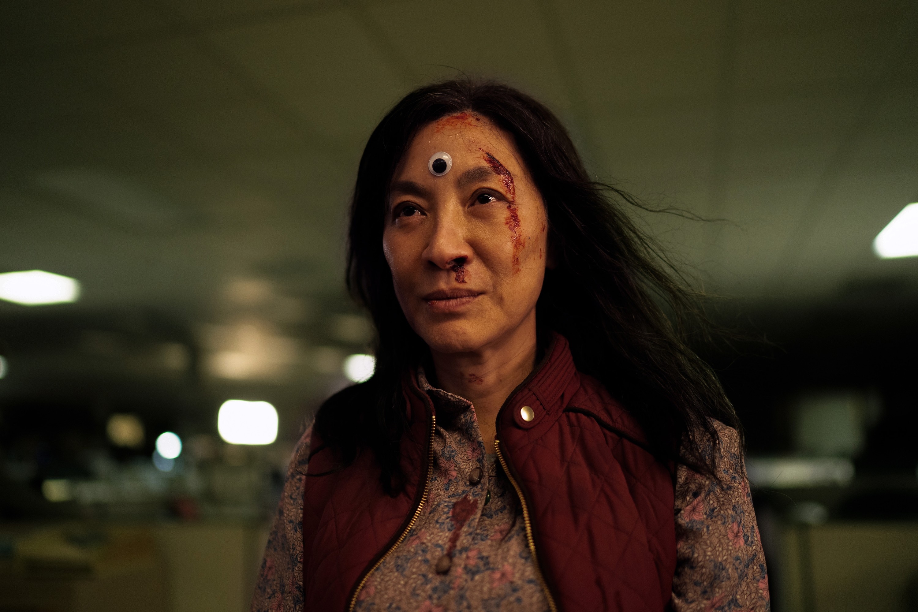 Michelle Yeoh in Everything Everywhere All At Wone with third eye on her forehead, appears determined and slightly disheveled, wearing a patterned shirt and vest