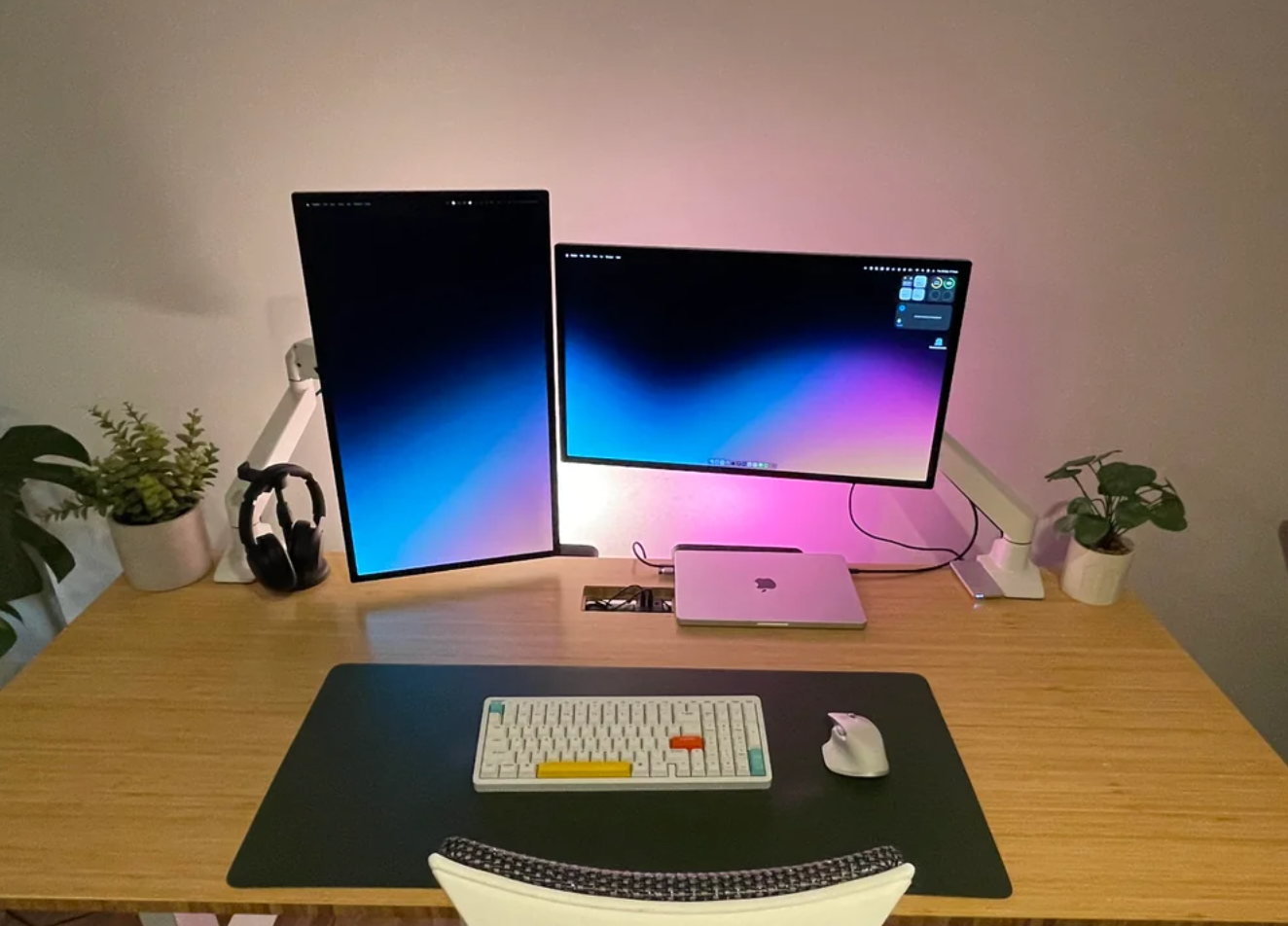 Desk setup with two monitors, a laptop, keyboard, mouse, and plants. Cozy workspace with a modern, minimalist design